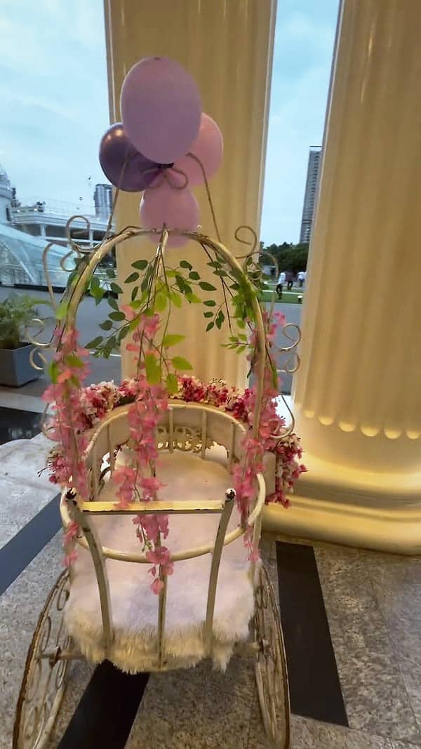 A white flower cart with pink blossoms and balloons at a venue entrance