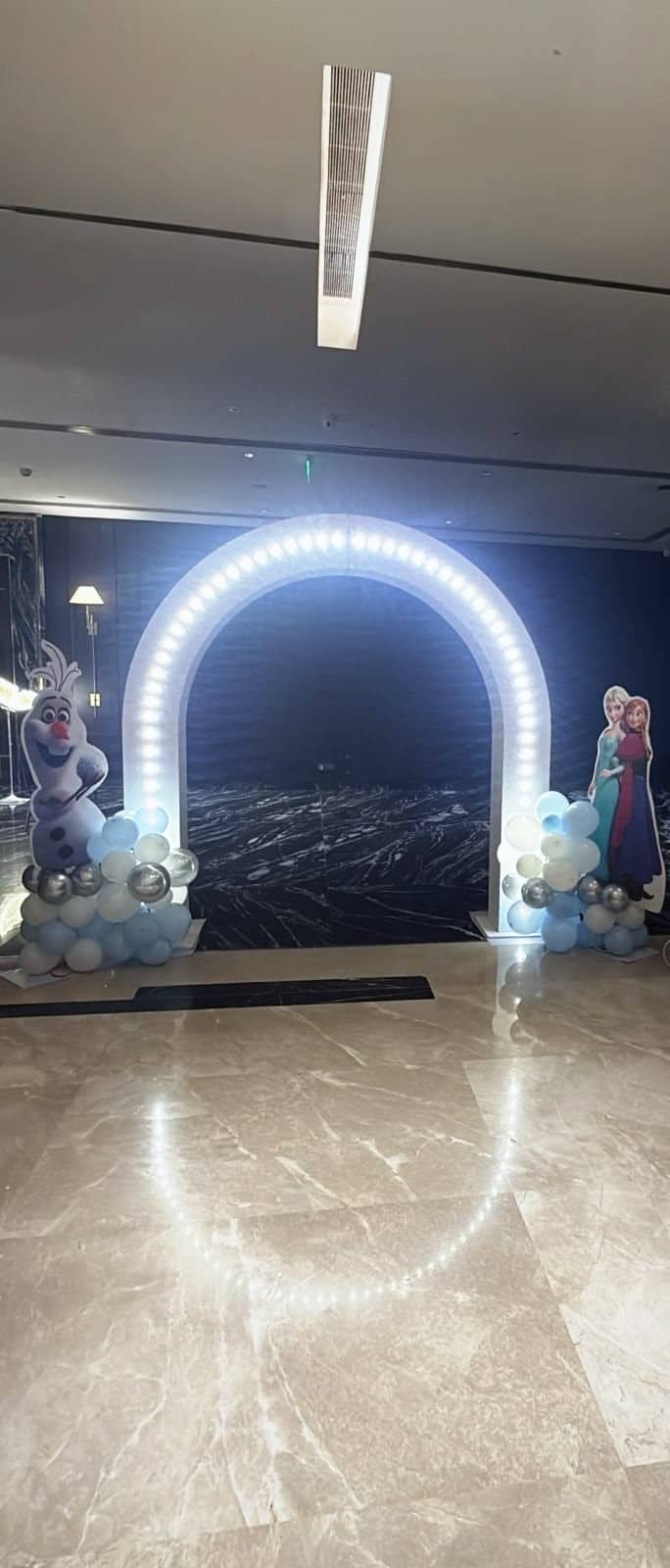 A glowing ring-light arch flanked by Olaf, Elsa and Anna cut-outs in a marble hotel foyer