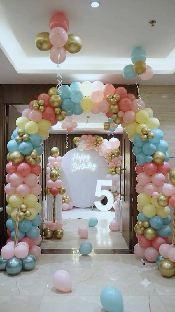 A pastel and gold balloon arch leading to a Happy Birthday backdrop