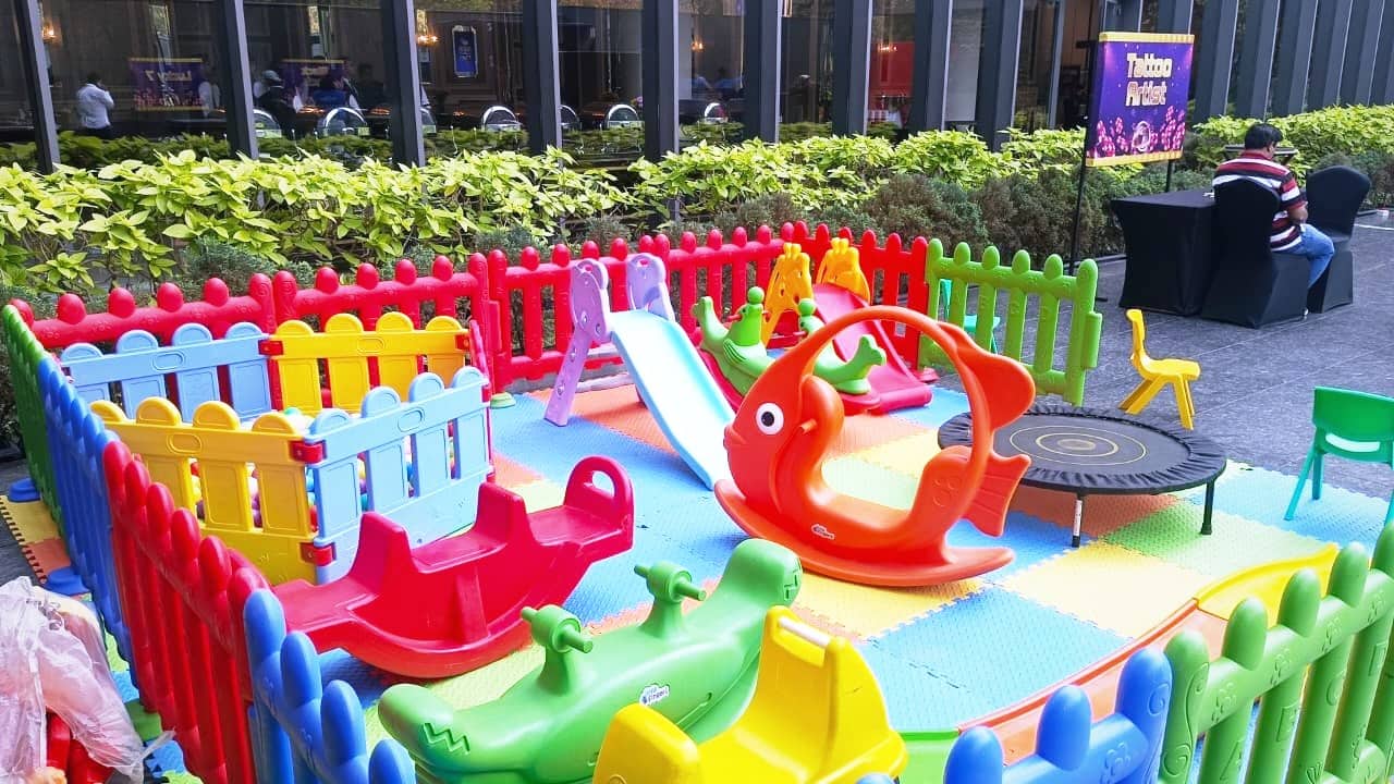 A garden soft play area with a slide, see-saw and colourful play fencing