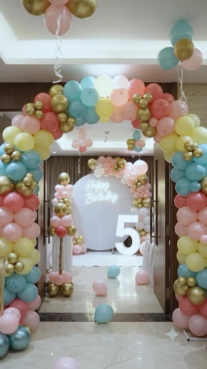 A pastel and gold balloon tunnel leading to a Happy Birthday backdrop