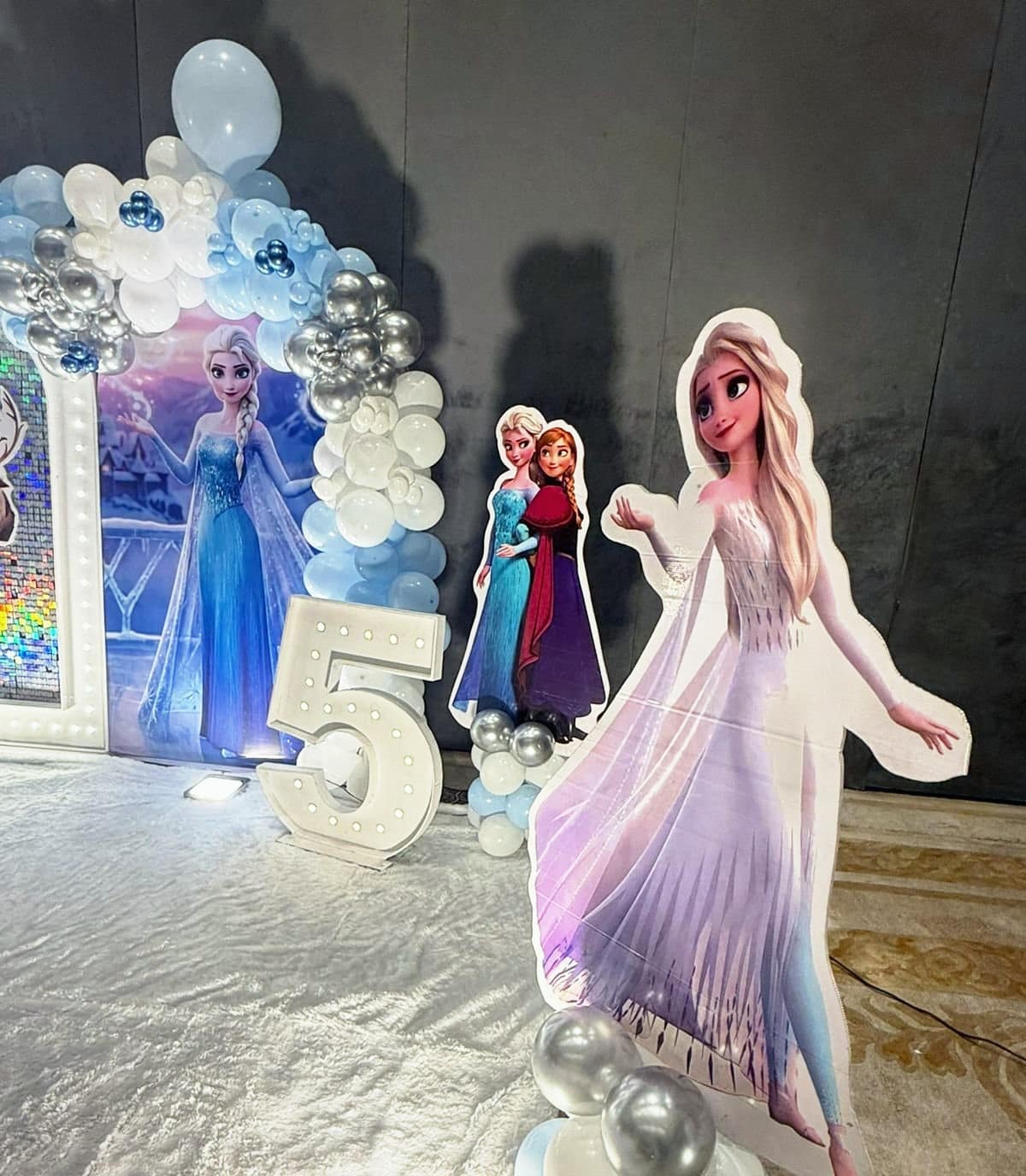 A Frozen stage with Elsa and Anna cut-outs, a lit number five and a snow-white floor