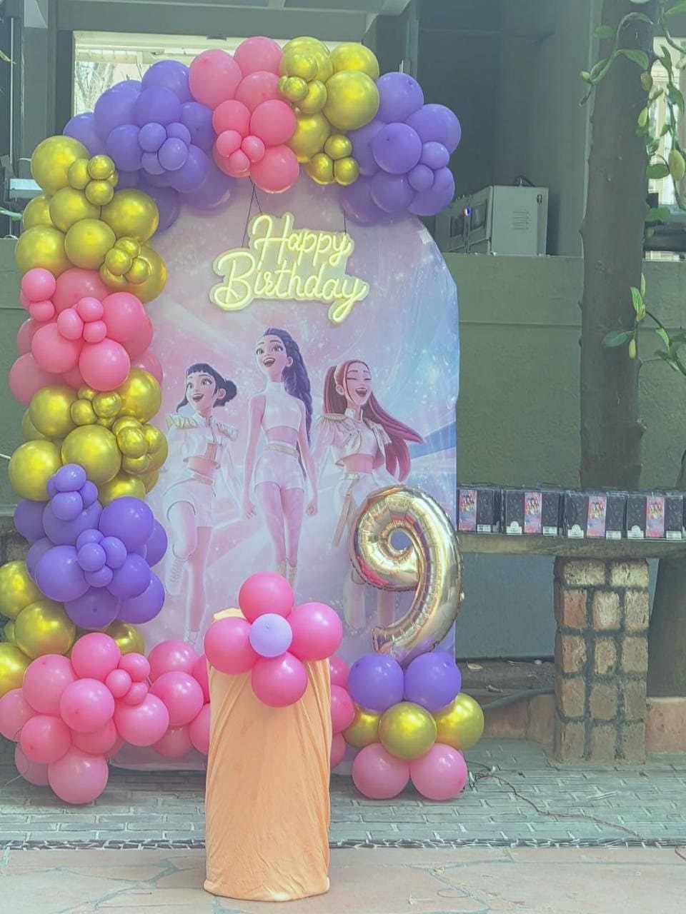 A K-pop backdrop framed by pink, purple and gold balloons with a gold number nine