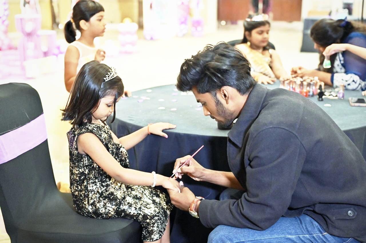 A nail artist painting a young guest’s nails at a party table