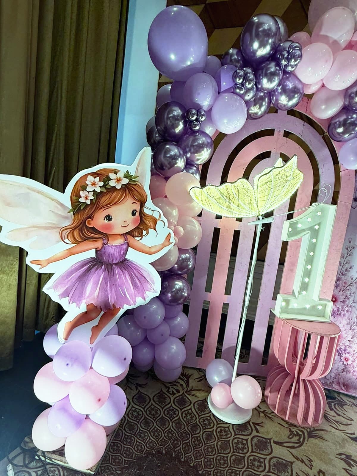 A lilac balloon arch with a fairy cut-out and a lit number one